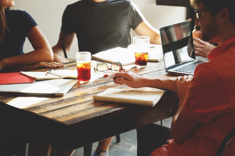 a group of people sitting around a table with laptops and papers on it